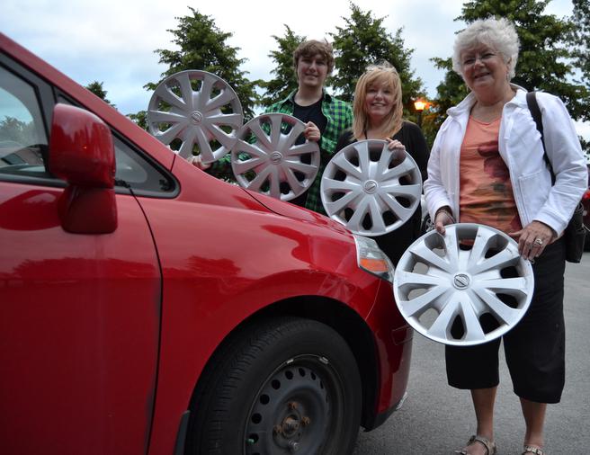 Dianne McDonald (right), along with her daughter-in-law Jacqueline (centre) and grandson Connor (right) pose with the four hubcaps a mysterious hubcap benefactor left for Dianne one July evening at DeWolf Park, next to her hubcap-less tire. (Chris Muise)